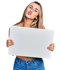 Fototapeta premium Hispanic young woman holding blank empty banner looking at the camera blowing a kiss being lovely and sexy. love expression.