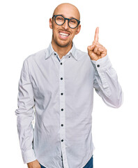 Bald man with beard wearing business shirt and glasses showing and pointing up with finger number one while smiling confident and happy.