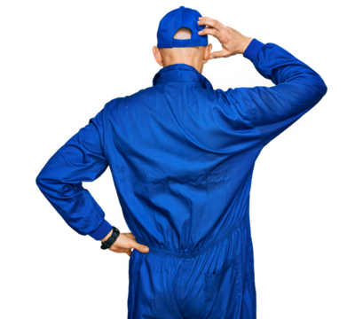 Bald man with beard wearing builder jumpsuit uniform backwards thinking about doubt with hand on head - Powered by Adobe