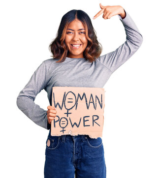 Young beautiful mixed race woman holding woman power banner pointing finger to one self smiling happy and proud