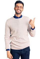 Naklejka premium Young handsome hispanic man wearing elegant clothes and glasses smiling with happy face looking and pointing to the side with thumb up.