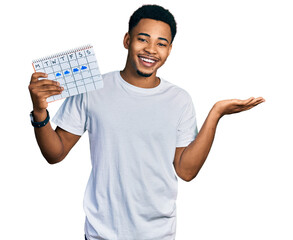 Young african american man holding rainy weather calendar celebrating victory with happy smile and winner expression with raised hands