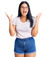 Young beautiful asian girl wearing casual clothes and glasses celebrating crazy and amazed for success with arms raised and open eyes screaming excited. winner concept