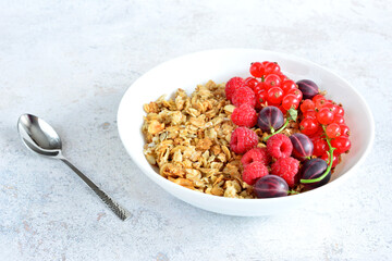 granola with raspberry, gooseberry and red currant in white plate with spoon