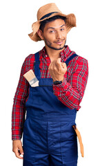 Handsome latin american young man weaing handyman uniform beckoning come here gesture with hand inviting welcoming happy and smiling