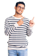 Hispanic handsome young man wearing casual clothes and glasses smiling and looking at the camera pointing with two hands and fingers to the side.