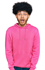 Young african american man with afro hair wearing casual pink sweatshirt afraid and shocked with surprise and amazed expression, fear and excited face.