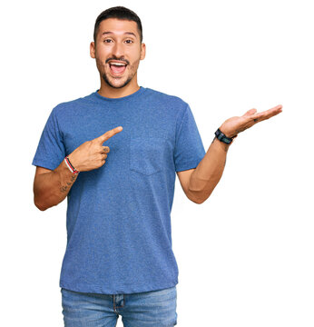 Handsome man with tattoos wearing casual clothes amazed and smiling to the camera while presenting with hand and pointing with finger.
