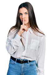 Young brunette teenager wearing business white shirt asking to be quiet with finger on lips. silence and secret concept.