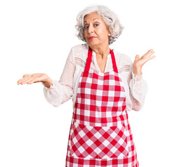 Senior grey-haired woman wearing apron clueless and confused expression with arms and hands raised. doubt concept.