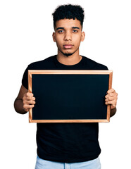 Young african american man holding blackboard thinking attitude and sober expression looking self confident