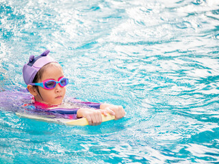 Asian child or kid girl wearing swimming suit to learning on swimming pool , learn and training swim on kick board