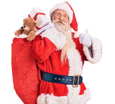 Old senior man with grey hair and long beard wearing santa claus costume holding bag with presents smiling happy and positive, thumb up doing excellent and approval sign
