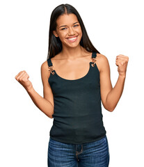 Beautiful hispanic woman wearing casual clothes very happy and excited doing winner gesture with...