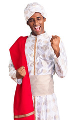 African handsome man wearing tradition sherwani saree clothes celebrating surprised and amazed for success with arms raised and eyes closed. winner concept.