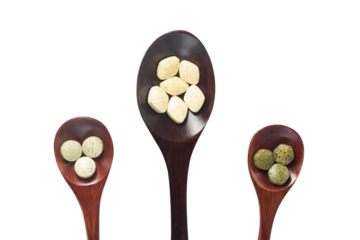 Multivitamins, multimineral, and phytonutrients are pressed tablets as nutritional supplements placed on a big wooden spoon and small wooden spoon with a transparent background.