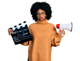 Young african american woman holding video film clapboard and megaphone relaxed with serious expression on face. simple and natural looking at the camera.