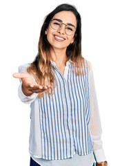 Beautiful hispanic woman wearing casual striped shirt smiling friendly offering handshake as greeting and welcoming. successful business.