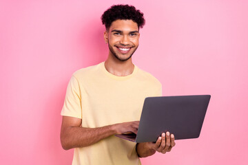 Photo of cheerful toothy beaming intelligent guy dressed yellow stylish t-shirt texting email on laptop isolated on pink color background
