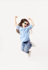 Portrait of smiling cute little toddler girl in blue casual outfit. child in funny glasses jumping isolated over white background. Looking at camera and laughs