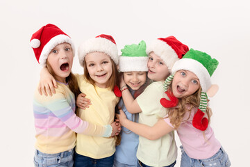 Merry Christmas and Happy New Year! A group of cheerful happy children in festive santa claus and elf hats on a white studio background. Children hug and have fun