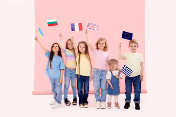 Cute little children holding in  hands the flags of the European countries,  democratic Union  on a pink background. The concept of supporting the union of states in war