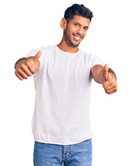 Young latin man wearing casual clothes approving doing positive gesture with hand, thumbs up smiling and happy for success. winner gesture.