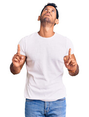 Fototapeta premium Young latin man wearing casual clothes pointing up looking sad and upset, indicating direction with fingers, unhappy and depressed.