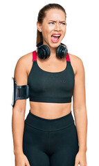 Beautiful blonde woman wearing gym clothes and using headphones angry and mad screaming frustrated and furious, shouting with anger. rage and aggressive concept.