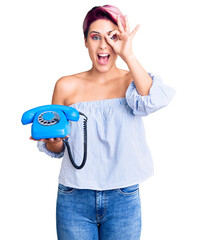 Young beautiful woman with pink hair holding vintage telephone smiling happy doing ok sign with hand on eye looking through fingers