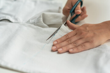 Shortening jeans. White jeans, Measuring tape, scissors on table. Jeans cutting.