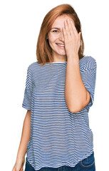 Young caucasian woman wearing casual clothes covering one eye with hand, confident smile on face and surprise emotion.