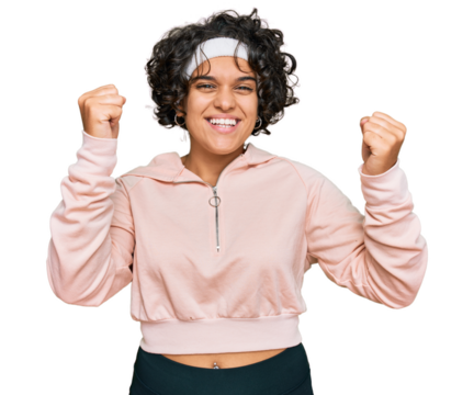 Young hispanic woman with curly hair wearing sportswear screaming proud, celebrating victory and success very excited with raised arms - Powered by Adobe