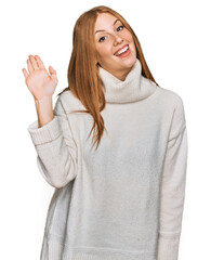 Young irish woman wearing casual winter sweater waiving saying hello happy and smiling, friendly welcome gesture
