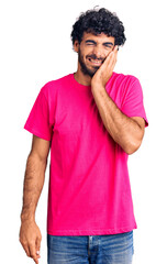 Handsome young man with curly hair and bear wearing casual pink tshirt touching mouth with hand with painful expression because of toothache or dental illness on teeth. dentist