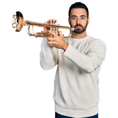 Young hispanic man with beard playing trumpet relaxed with serious expression on face. simple and...