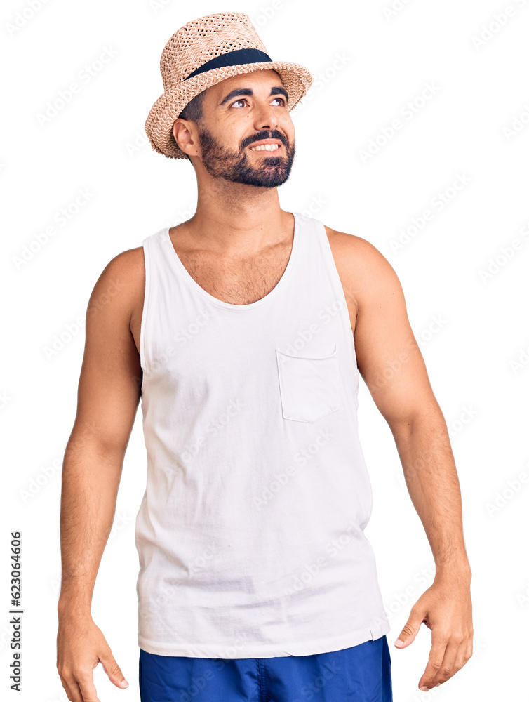 Wall mural Young hispanic man wearing casual summer hat looking away to side with smile on face, natural expression. laughing confident.