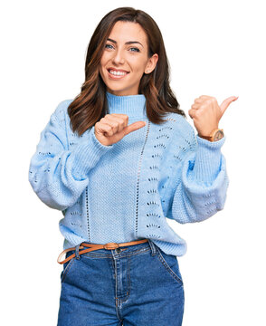 Young brunette woman wearing casual winter sweater pointing to the back behind with hand and thumbs up, smiling confident