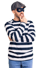 Fototapeta premium Young handsome man wearing burglar mask thinking worried about a question, concerned and nervous with hand on chin