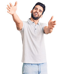 Young handsome man with beard wearing casual polo looking at the camera smiling with open arms for hug. cheerful expression embracing happiness.