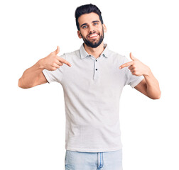 Young handsome man with beard wearing casual polo looking confident with smile on face, pointing...