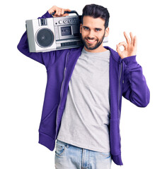 Young handsome man with beard listening to music using vintage boombox doing ok sign with fingers, smiling friendly gesturing excellent symbol