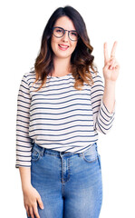 Beautiful young brunette woman wearing casual clothes and glasses showing and pointing up with fingers number two while smiling confident and happy.