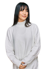 Fototapeta premium Young brunette woman with bangs wearing casual turtleneck sweater looking away to side with smile on face, natural expression. laughing confident.