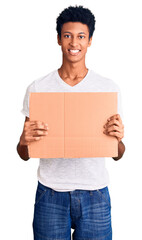 Young african american man holding banner cardboard looking positive and happy standing and smiling with a confident smile showing teeth