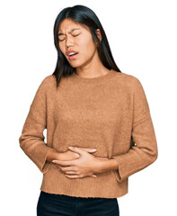 Beautiful young asian woman wearing casual winter sweater with hand on stomach because nausea, painful disease feeling unwell. ache concept.