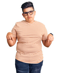 Little boy kid wearing casual clothes and glasses pointing down looking sad and upset, indicating direction with fingers, unhappy and depressed.