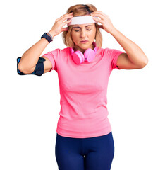 Young blonde woman wearing sportswear and headphones suffering from headache desperate and stressed because pain and migraine. hands on head.