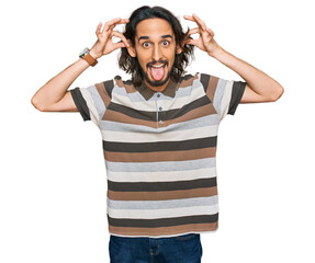 Young hispanic man wearing casual clothes smiling pulling ears with fingers, funny gesture....