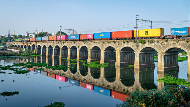 Pune, Maharashtra, India-June 1st, 2023: Colorful container train passing over bridge with nice reflection in river water.